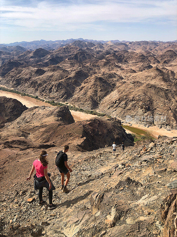 孩子们在贫瘠的山地上徒步旅行，山下有河流峡谷