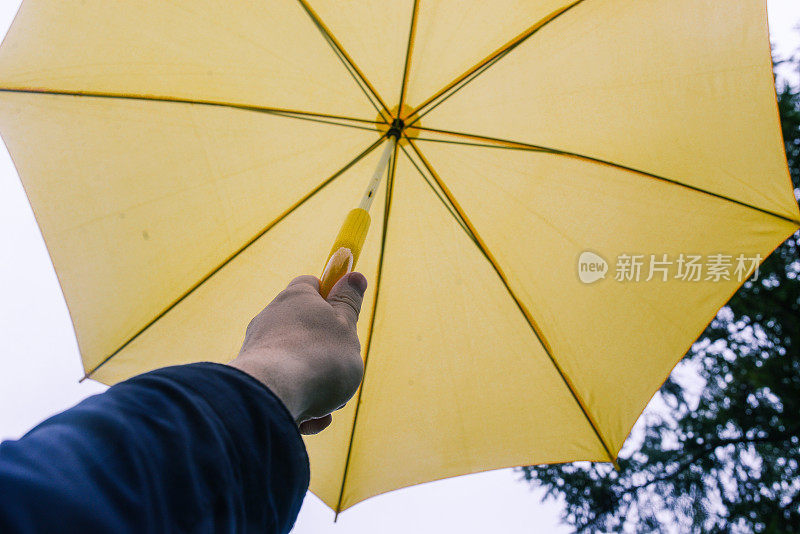 男人的手拿着一把黄色的伞。秋天的雨天。灰色的天空。天气预报的概念。秋天背景