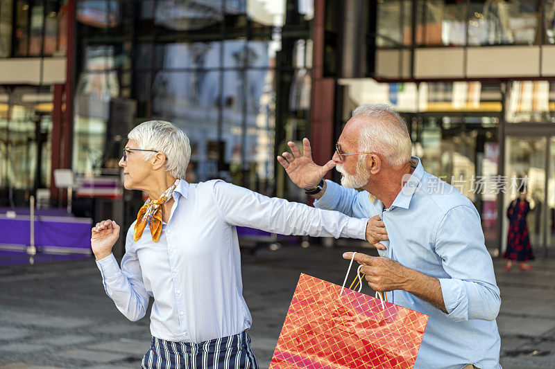 一对拿着购物袋的老夫妇在逛完购物中心后进行了一场激烈的对话