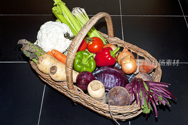 各种颜色的新鲜蔬菜装在柳条篮子里，铺在黑色瓷砖地板上