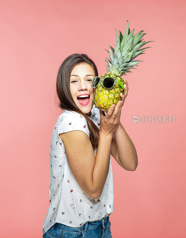 快乐的年轻女子拿着菠萝与太阳镜在珊瑚的背景