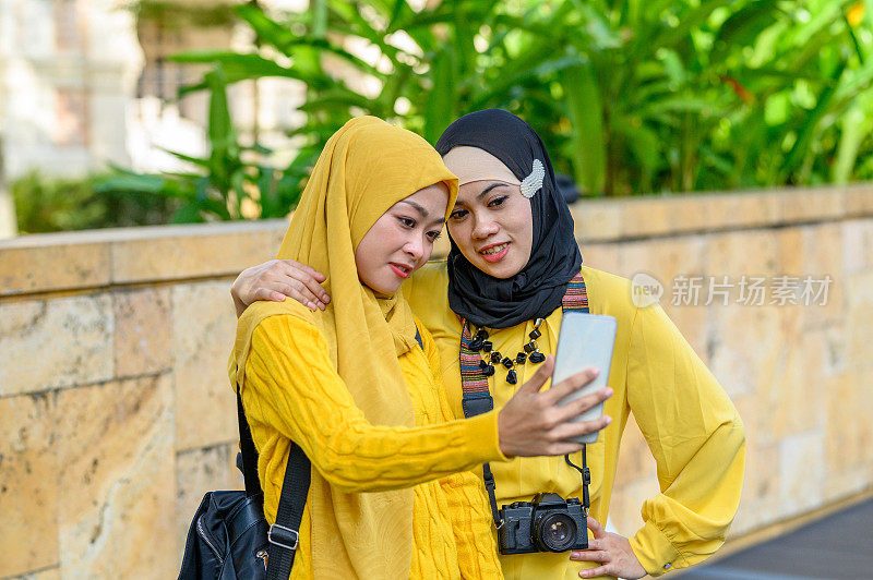 两名穆斯林女性旅行者戴着头巾自拍与她的智能手机在城市街道上