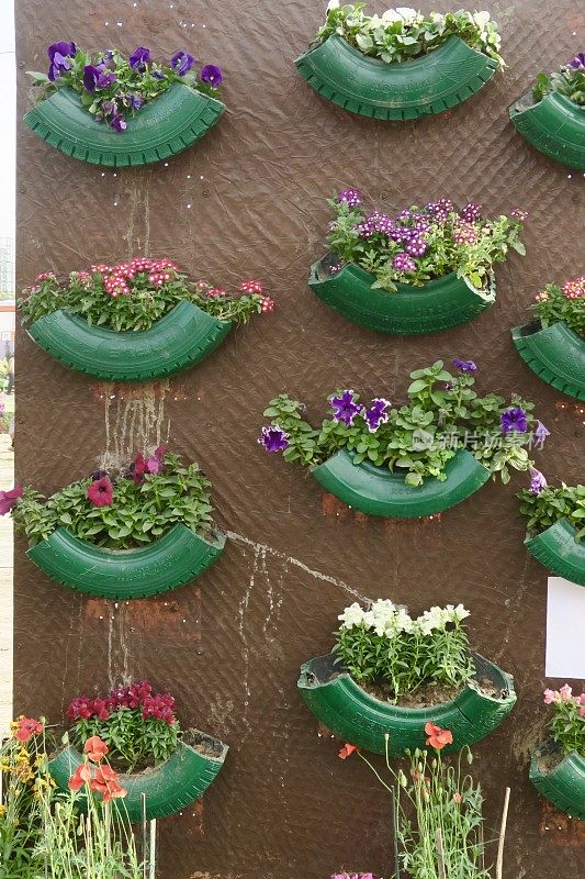 形象的垂直墙花园采用再生橡胶汽车轮胎部分作为花盆，升级管填充土壤和植物，涂绿色并组装在柱设计，环保和节省空间的花园设计理念