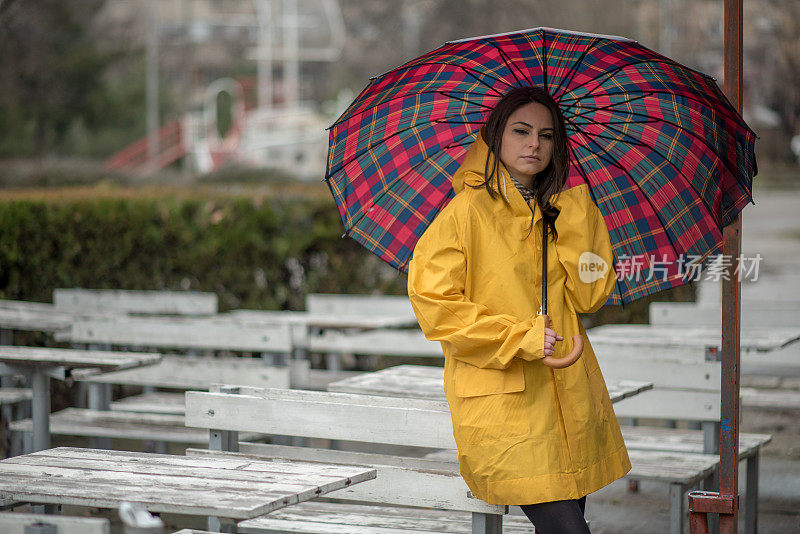 穿着黄色雨衣的年轻女子在公园里度过雨天