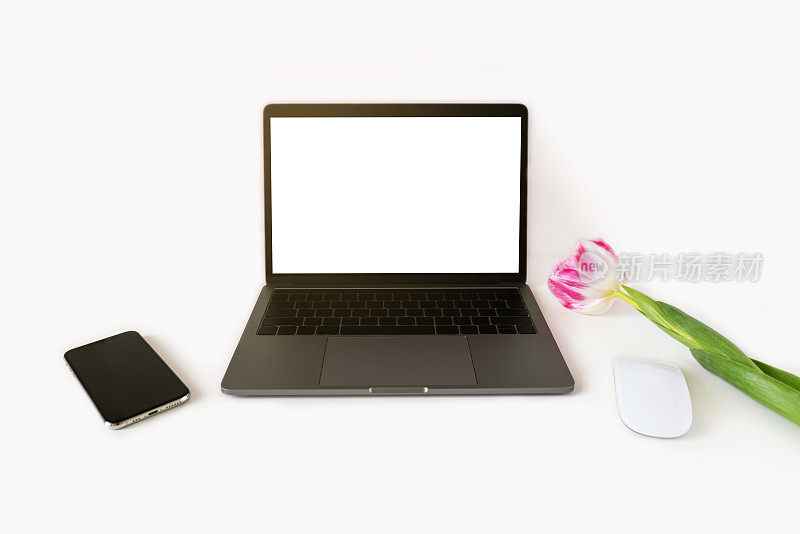 白色的工作台，打开的笔记本电脑和鼠标，智能手机和粉红色的郁金香。