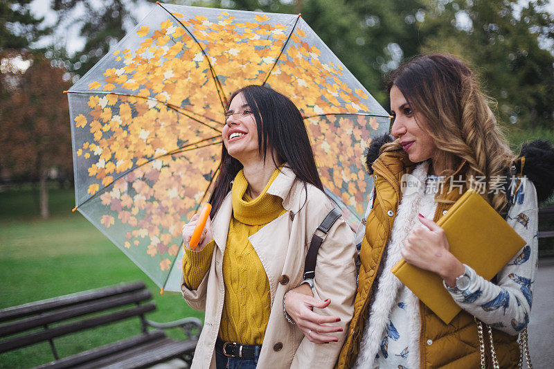 快乐的女孩们在雨天穿过公园