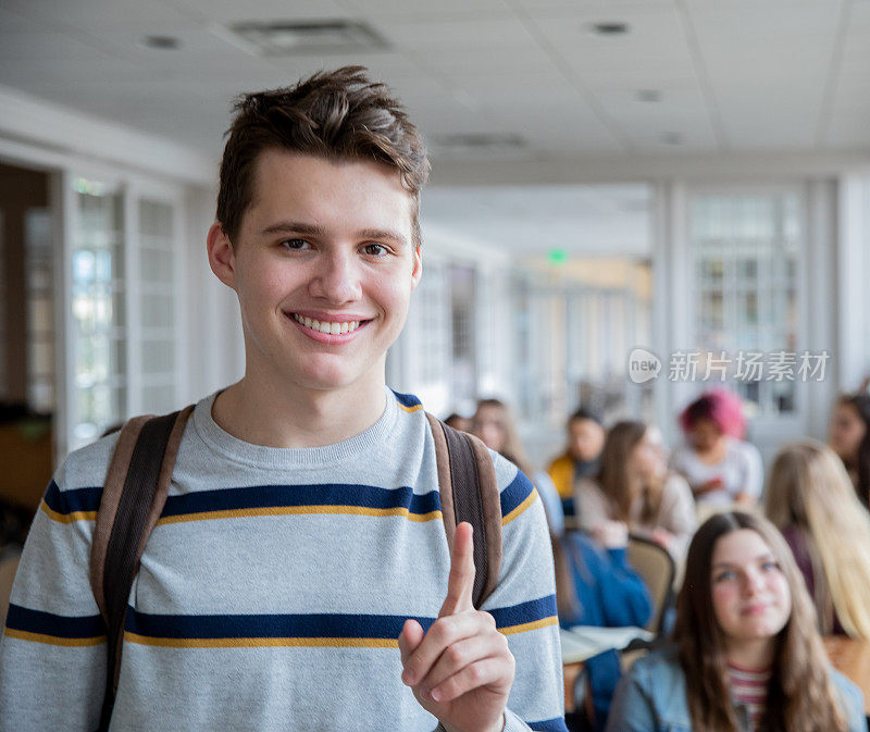一名男生站在满教室的学生面前，举起他的食指