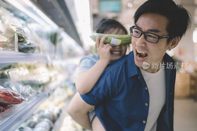 一位亚洲华人中年人背着他的女儿在超市挑选和购买冷藏蔬菜