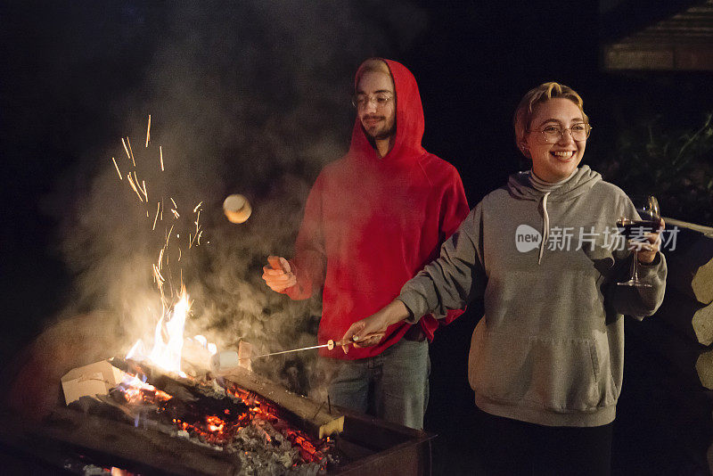 千禧一代夫妇晚上在户外的火上烤棉花糖。