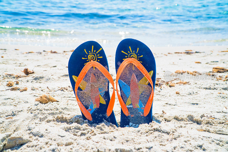蓝色和橙色的人字拖在蓝色和水晶般的海边在暑假。理想的广告旅游，假日和海滨胜地