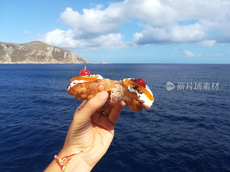 手与西西里cannolo与大海和Egadi岛的背景