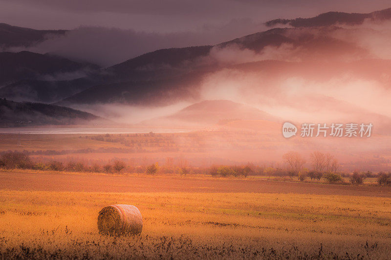 连绵起伏的风景:在保加利亚，一堆堆干草，在夕阳下收获，还有薄雾弥漫的巴尔干山脉