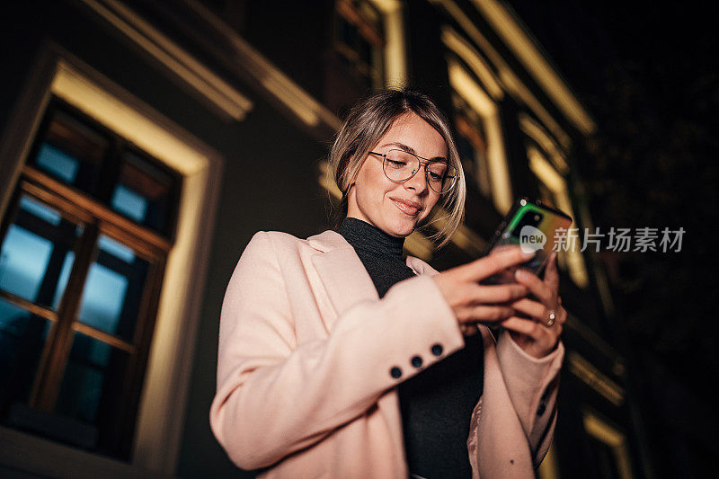 一个美丽的女人晚上在城市的户外使用手机