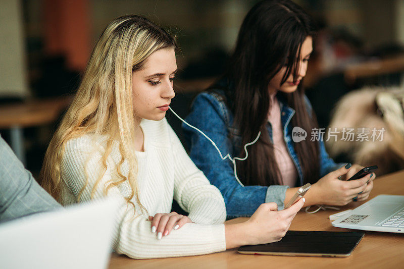 两个女生在图书馆使用平板电脑和笔记本电脑。和听音乐