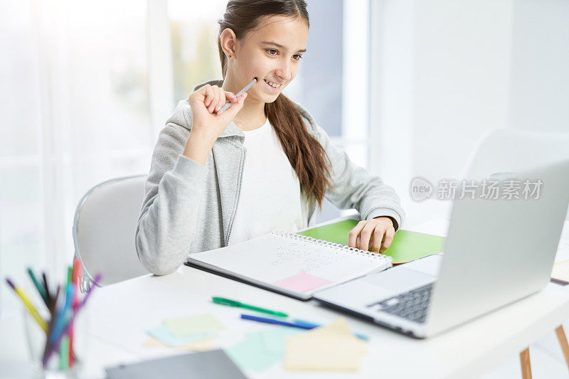 在线课堂。开朗的拉丁少女微笑着，看着笔记本电脑屏幕，与她的老师交流，在家里上在线课