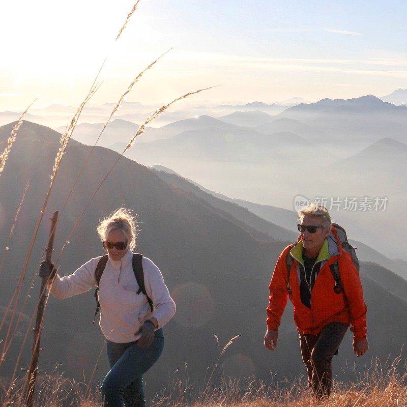 一对成熟的夫妇早晨沿着长满草的山坡徒步旅行