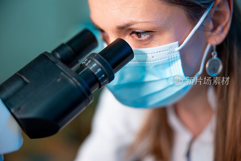 女性微生物学家戴防护面罩，透过显微镜观察
