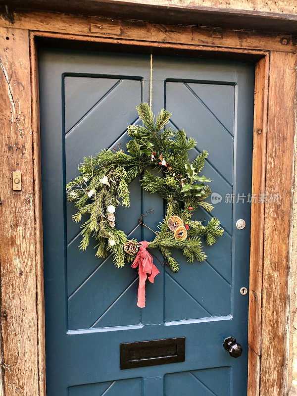 特写图像的木制面板前门与黑色信箱和冷杉圣诞花环装饰干柑橘，松果，冬青叶和浆果