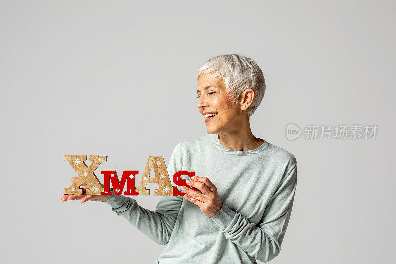 美丽的年长成熟的女人与灰色的头发装饰圣诞树与装饰是白色的毛衣和裤子的背景