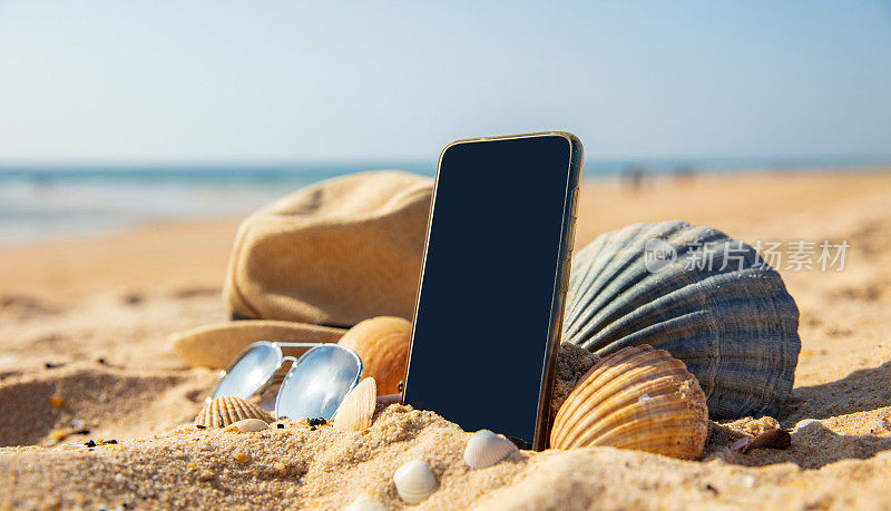 夏日度假概念，智能手机，太阳镜和帽子在海滩上