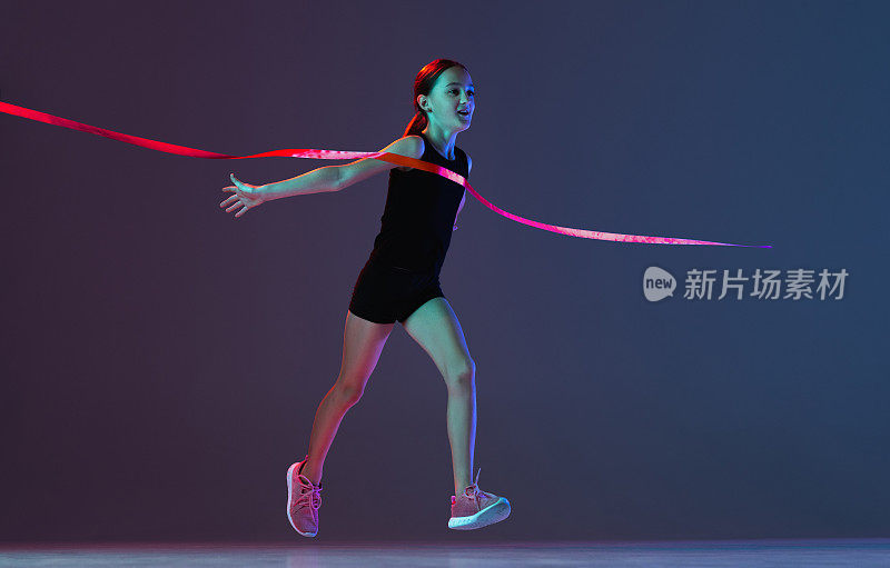 青春期女孩的全长肖像，运动员跨越红色丝带孤立的梯度蓝色紫色背景在霓虹灯。赢得