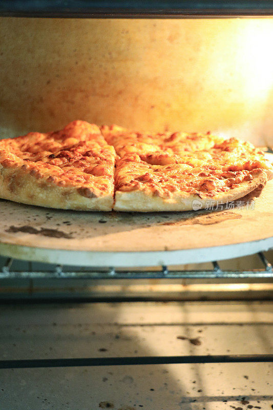 自制玛格丽塔披萨在烤箱里烘烤的特写图像，在披萨石头上烤脆的基底，磨碎的马苏里拉奶酪浇头，聚焦在前景
