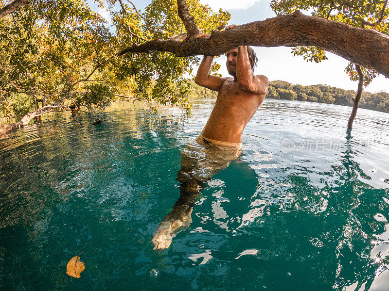 一个人挂在热带天然井的树上，尽情享受大自然