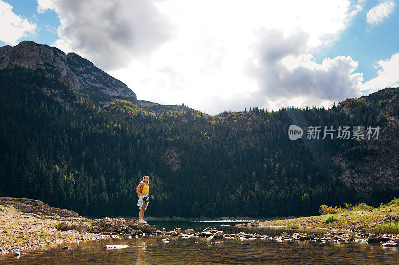 漂亮的女人背着背包在湖边散步。旅行的概念。