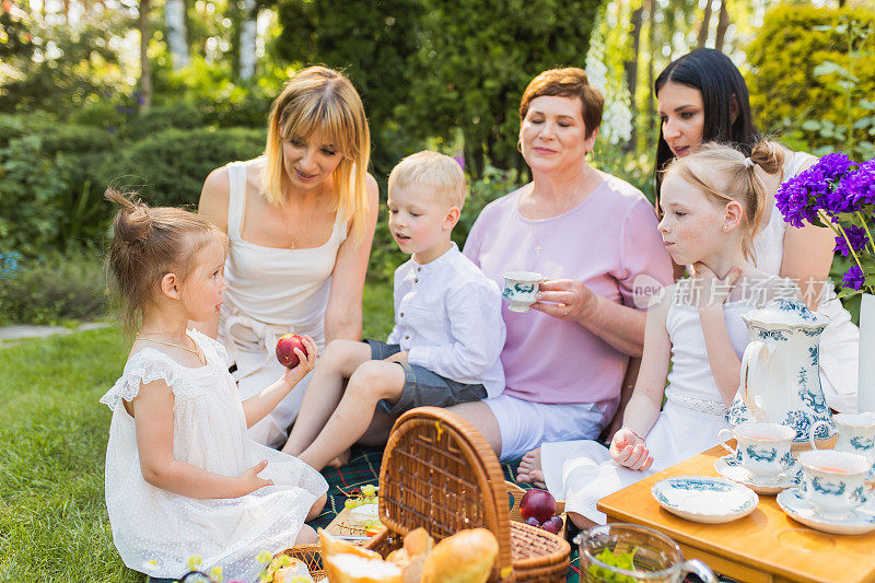 父母和孩子。奶奶和孙子。夏季野餐。户外娱乐。一家人围坐在一起吃一顿饭。两个女孩和男孩享受食物。休闲活动。假期