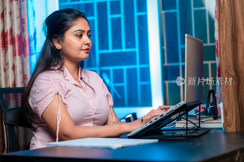 快乐的女人在笔记本电脑上打字，坐在家里办公室的桌子旁工作。
