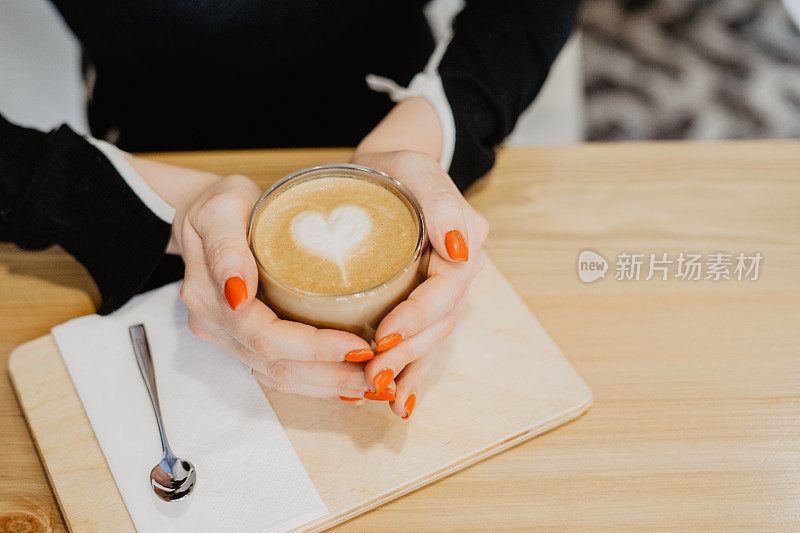 裁剪的女人手拿着一杯热拿铁咖啡在她的手。