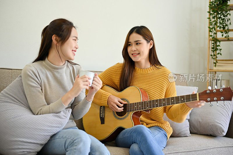 美丽的亚洲女性弹吉他和她的朋友唱歌，一起在家里玩。