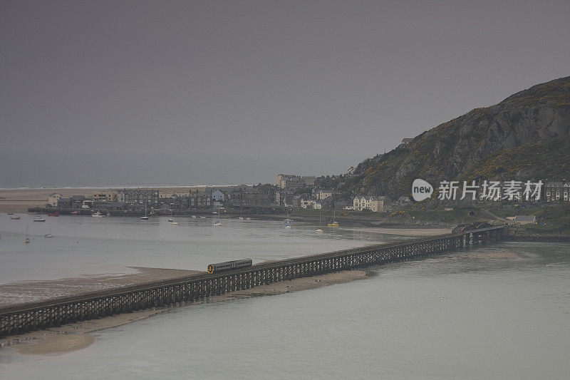 这条铁路在阴天穿过河口，背景是山丘和房屋