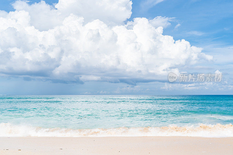 巴厘岛海滩场景-蓝绿色的印度洋，白色的沙子和蓝色的多云天空的背景。
