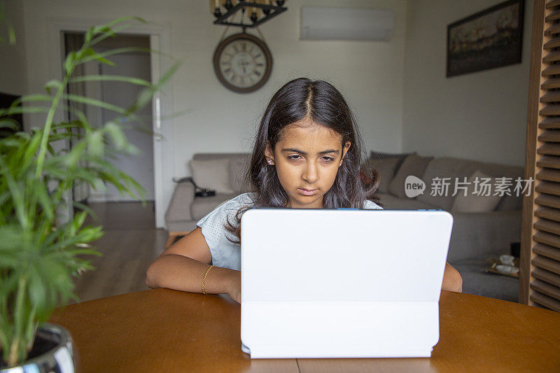 女孩坐在家里的桌子上做作业和使用数字平板电脑
