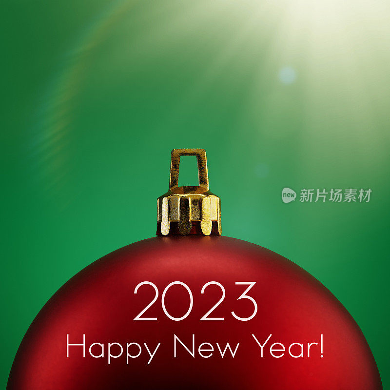 红色圣诞球在绿色背景与阳光和镜头耀斑与2023新年快乐的文字。假期，圣诞节和新年的概念