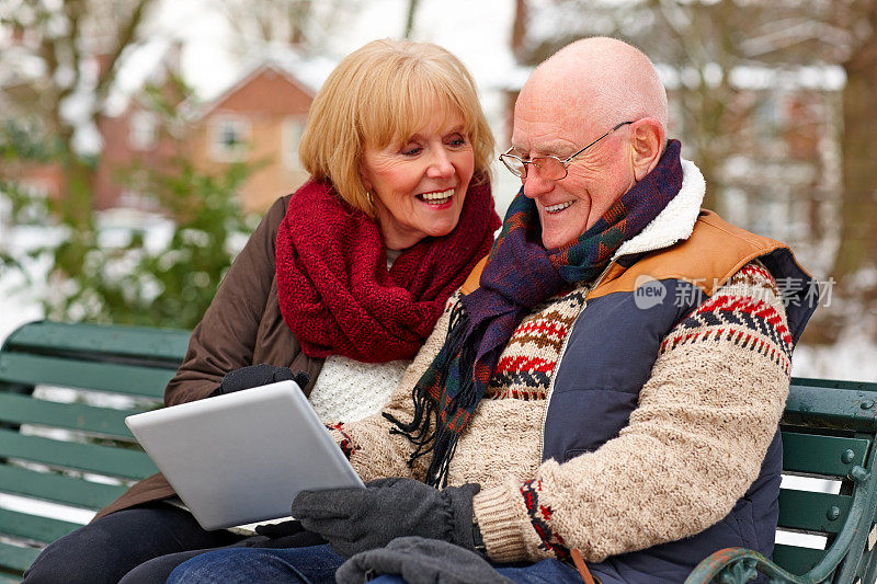 微笑的老夫妇穿着暖和的衣服使用数码平板电脑
