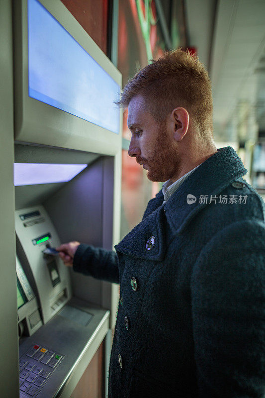 年轻的红发商人正在ATM机取款。