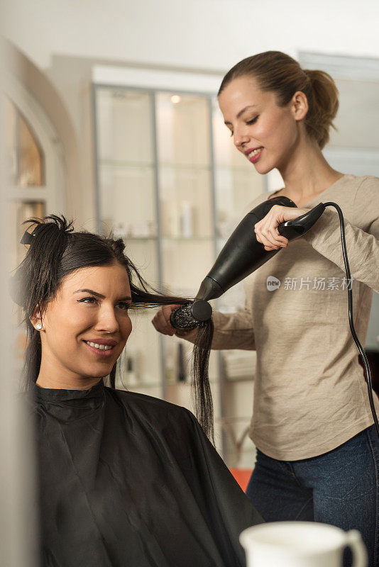 微笑的女人享受在发型师的头发干燥。