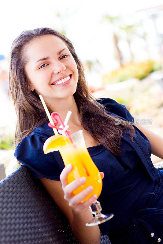 喝着橙汁坐在户外夏日咖啡馆里的年轻女子