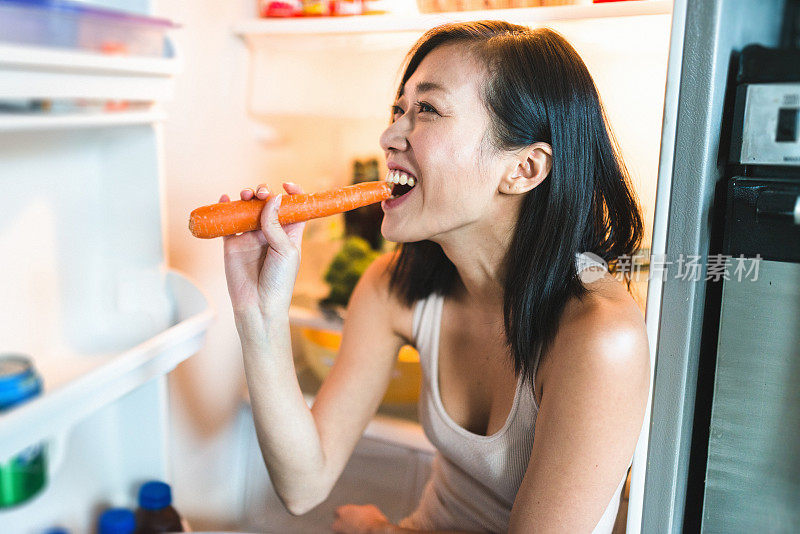 一个亚洲女人在厨房里笑着拿着打开的冰箱