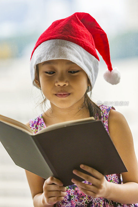 读书的年轻亚洲女孩戴着圣诞老人帽