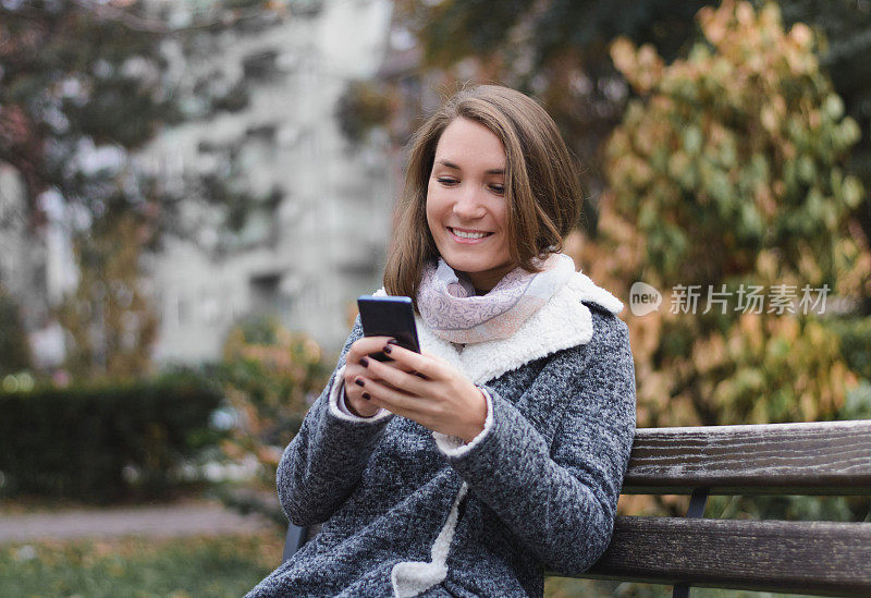 美丽的年轻女子使用手机在城市公园在秋天