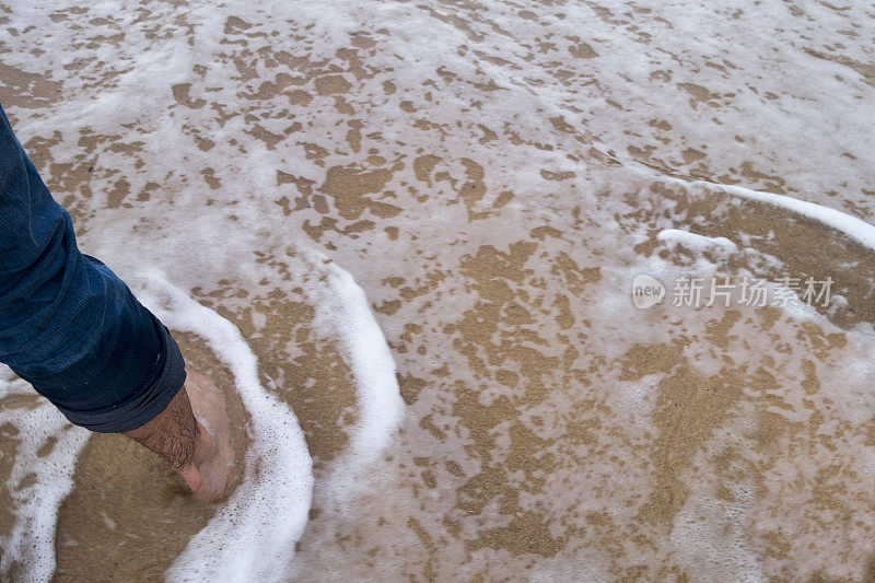 海滩上，脚踩在沙上，海浪淹没了沙滩