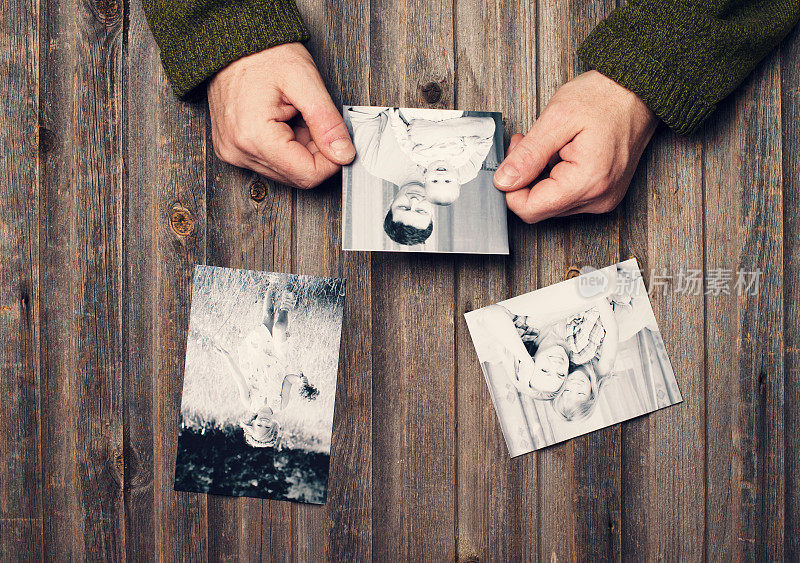家庭照片在男人手中和风化的木桌上。前视图。