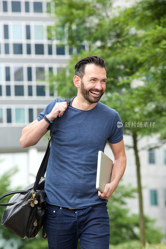 开朗的中年男人拿着手提包和笔记本电脑在户外散步
