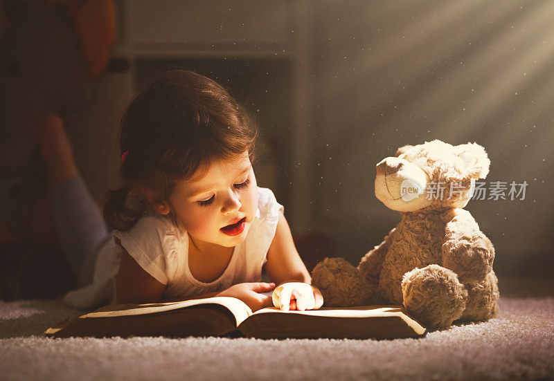 一个小女孩晚上在黑暗中和一只玩具熊一起看书