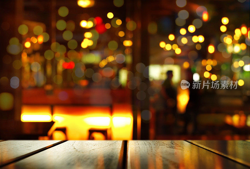 木质桌子的顶部有模糊的散景光和夜晚酒吧里人们的影子
