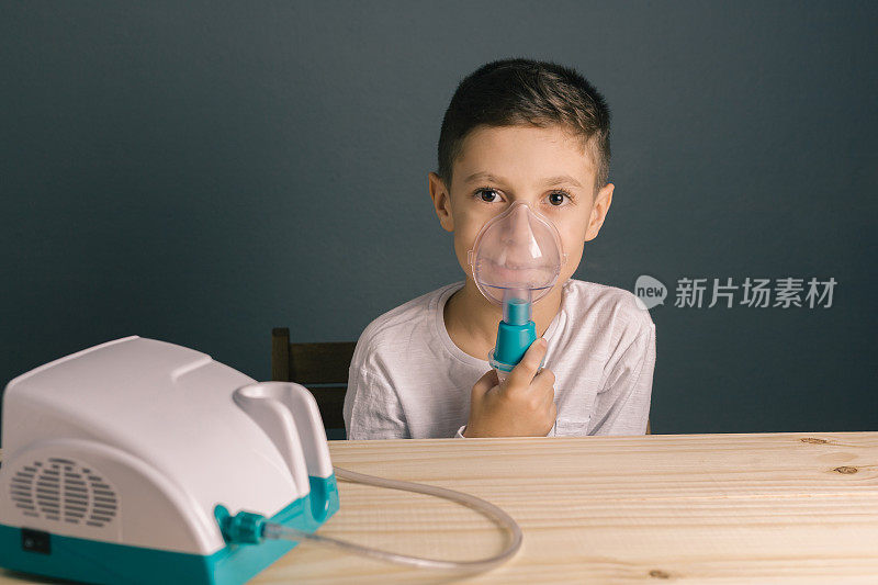 漂亮的病男孩吸入治疗口罩吸入器。一个可爱的小孩患有呼吸道疾病或哮喘。从氧气面罩看带有烟雾的喷雾器。