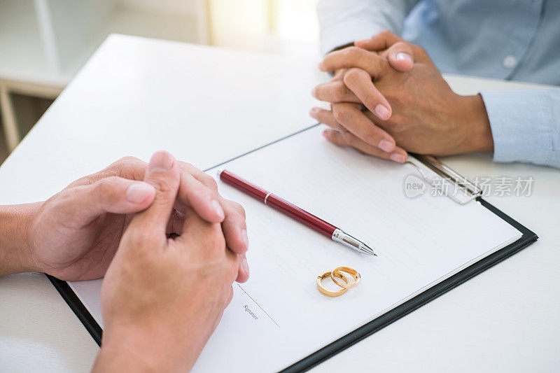 丈夫和妻子正在阅读离婚协议，签署离婚令(解除或取消婚姻)，提交离婚文件和两个金婚戒指